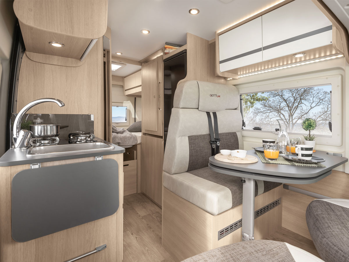 Innenaufnahem vom Wohnmobil giottiline t60 van, blick durch den van vorne links küchenzeile, auf dem bild rechts sitzplatz mit gedecktem tisch, blick nach hinten durch zu den einzelbetten